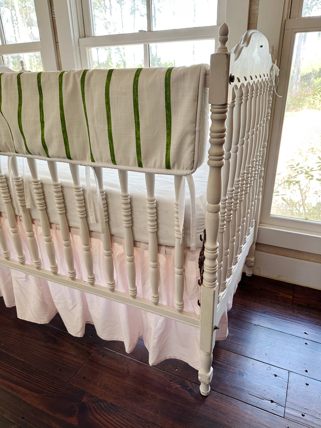 Corner view from the head of the crib, green stripes running the length of the long rail