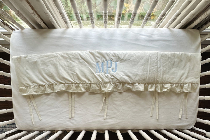 Overhead view of the monogrammed rail cover laid flat showing the gathered ruffle and tiny ties