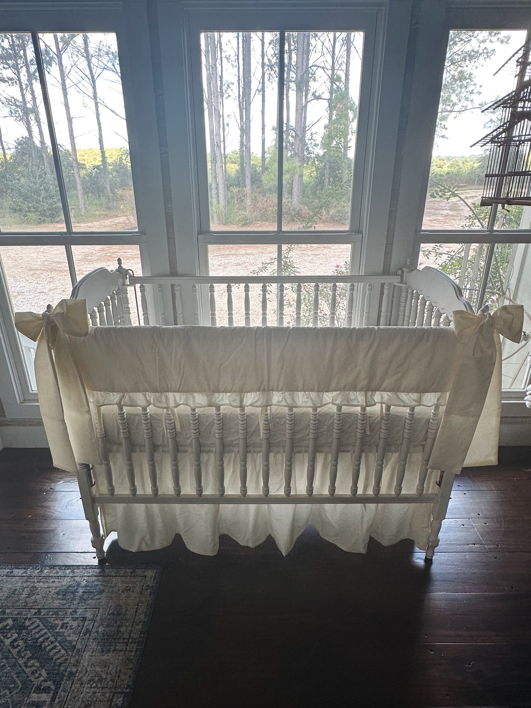 Backlit front view of the ivory ruffled rail cover set against three windows, farmhouse skirt falling to dark wood floors