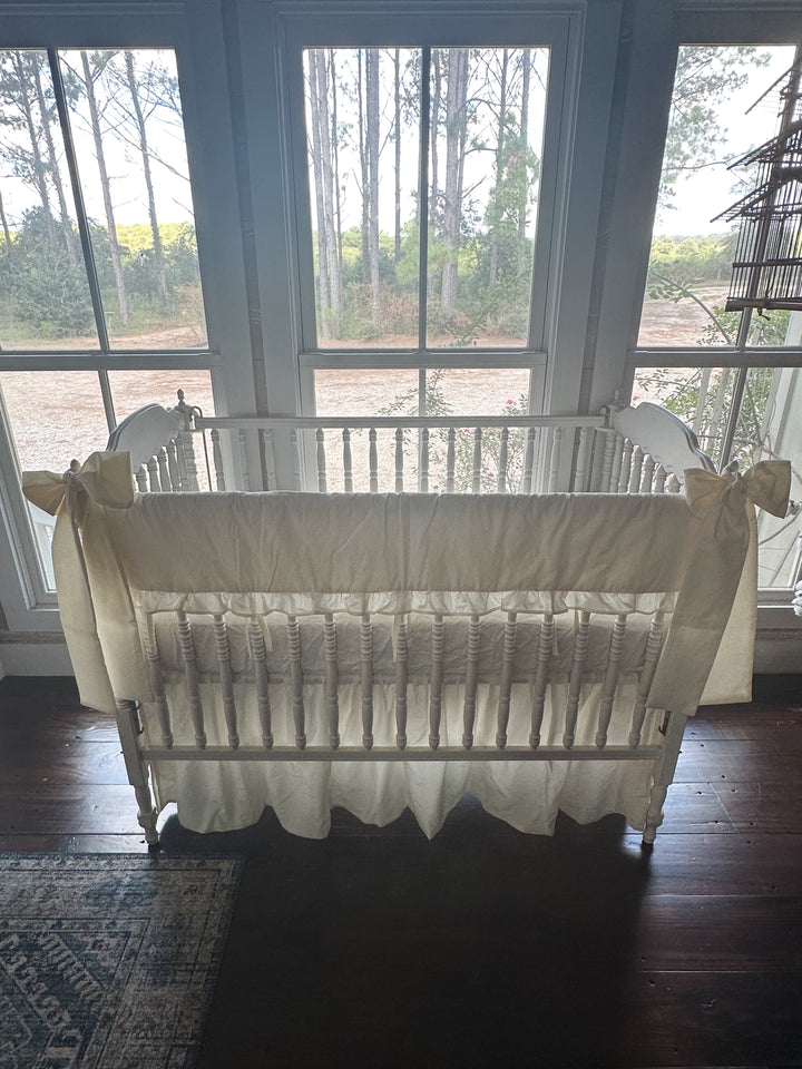 Backlit front view of the ivory ruffled rail cover set against three windows, farmhouse skirt falling to dark wood floors