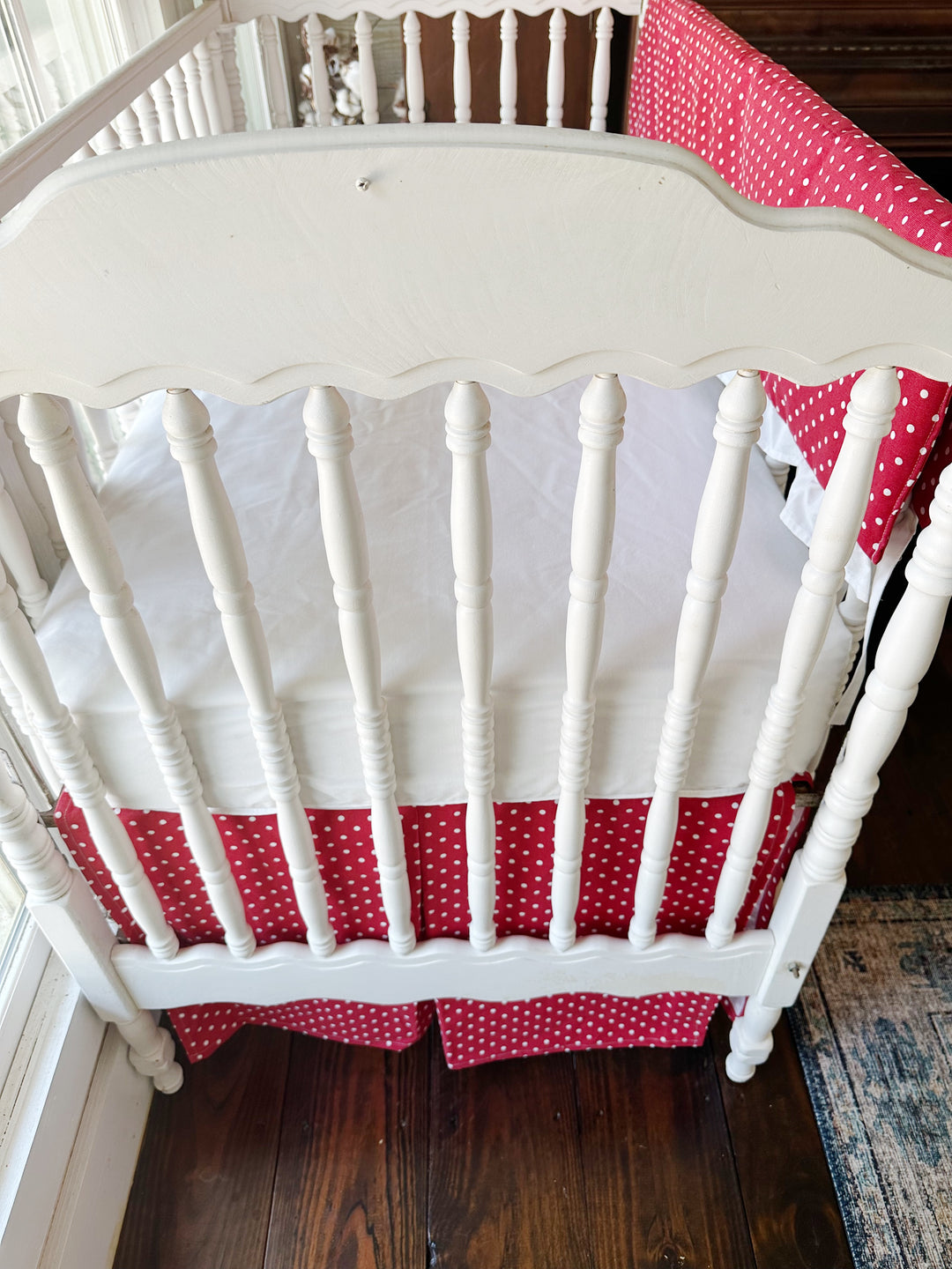 Looking down into the crib at the white sheet between the dotted rail cover and skirt
