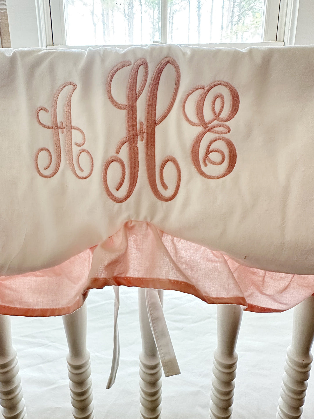 Pink three-initial script monogram embroidered on a white cotton scalloped crib rail cover