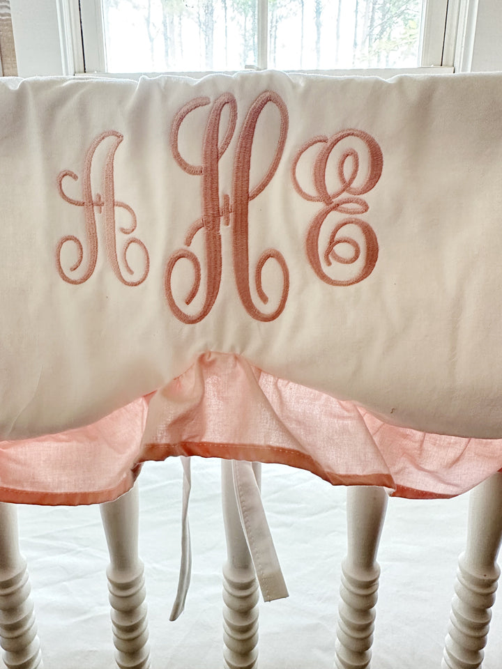 Pink three-initial script monogram embroidered on a white cotton scalloped crib rail cover