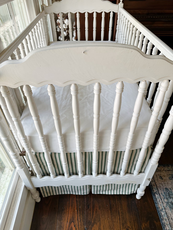 Seen from the end of the crib, the pleated ticking skirt beneath a plain white sheet