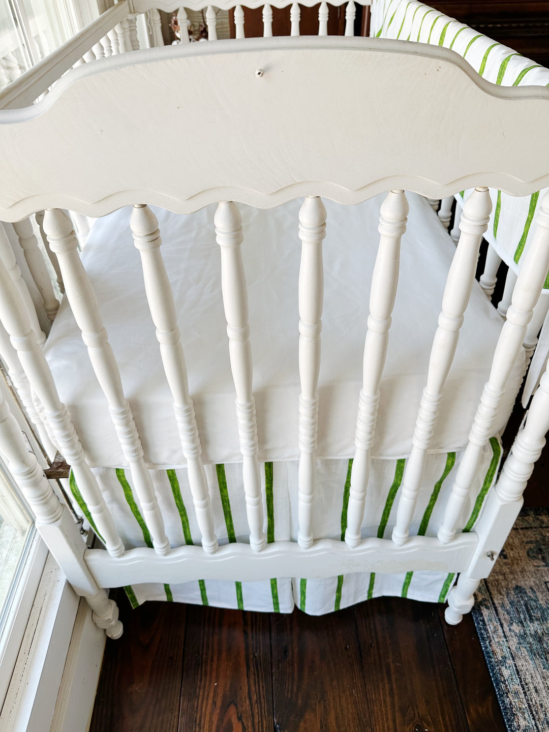 Head end of the crib from above, crisp white sheet over the green striped skirt