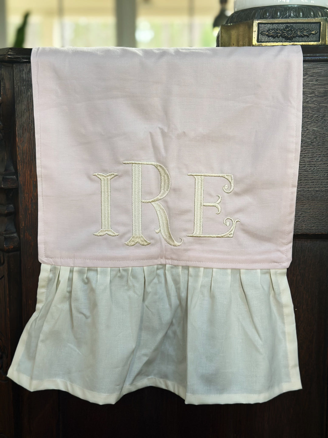 Close-up of a cream three-letter monogram embroidered on the baby pink runner just above the ivory ruffle