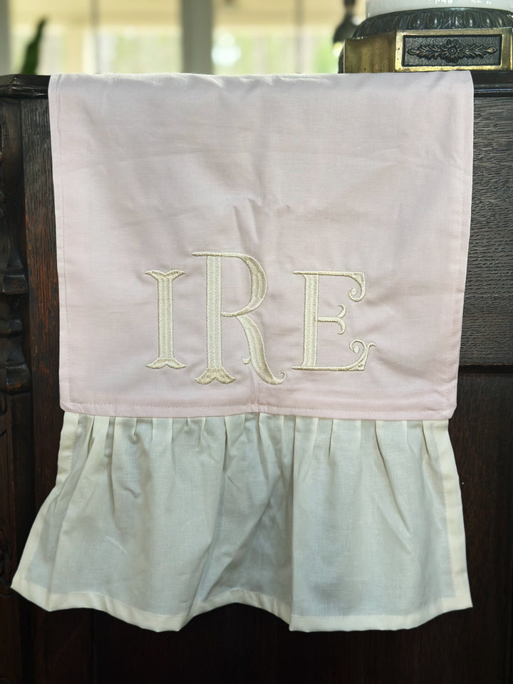 Close-up of a cream three-letter monogram embroidered on the baby pink runner just above the ivory ruffle