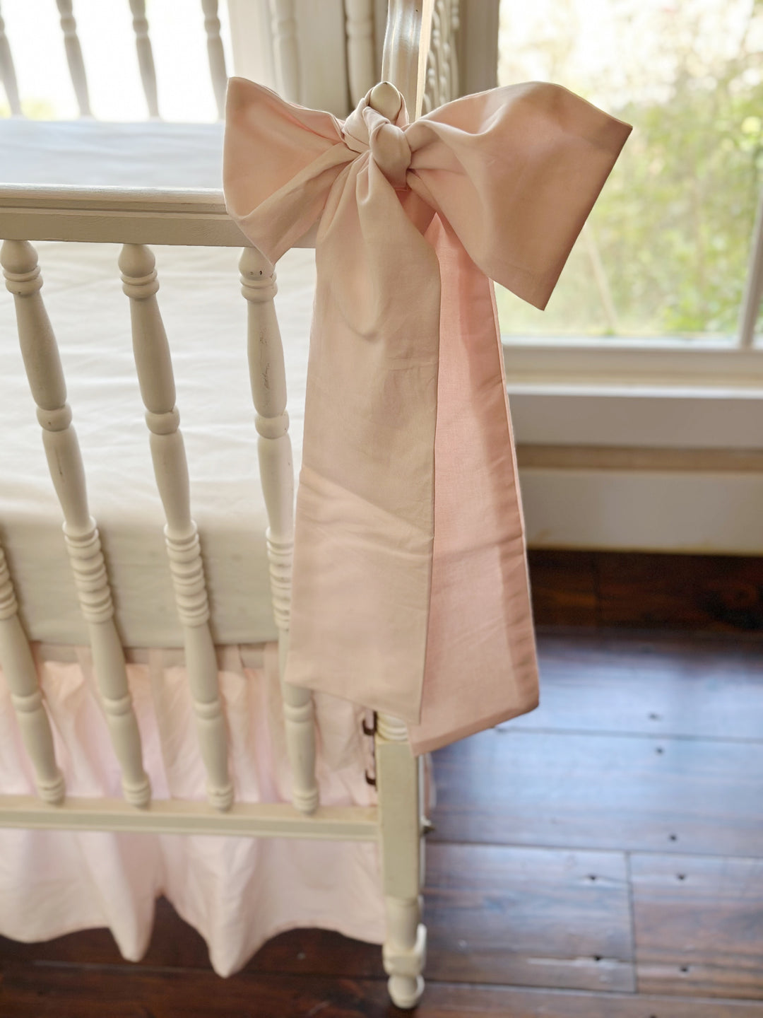 The tails of a pink sash against the turned spindles and the gathered skirt below