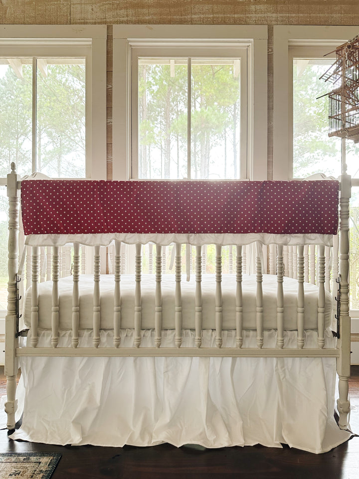 Straight-on view of the two-piece red polka dot crib set with white ties hanging between the spindles