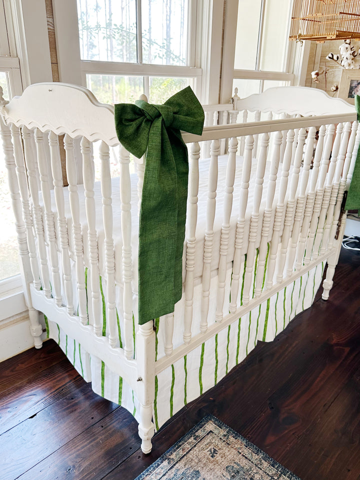 Angled view of the crib showing one green sash and the striped skirt running below the spindles