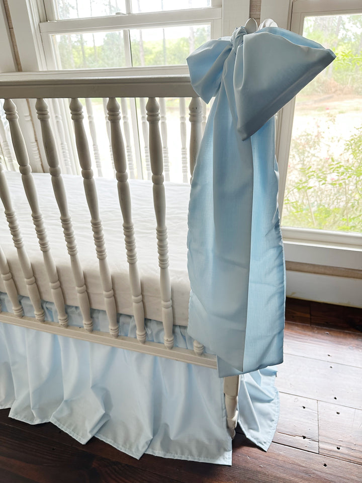 Large heirloom blue crib bow tied to the rail with long tails falling past the skirt