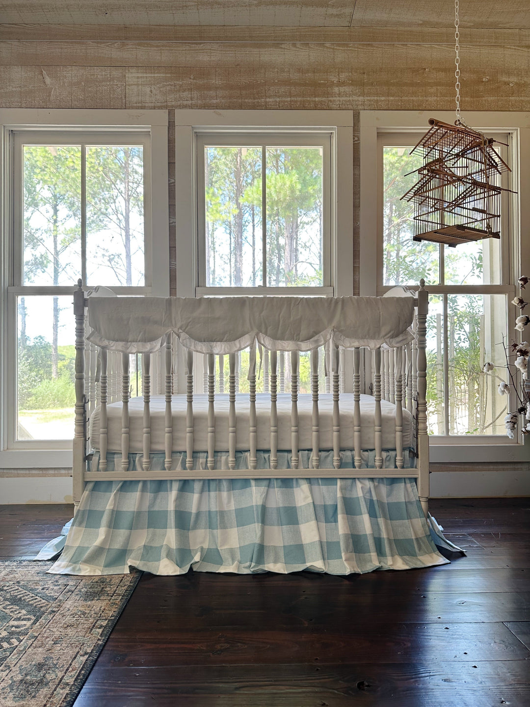 Blue buffalo check crib bedding set styled in a farmhouse nursery with shiplap walls and pine tree views
