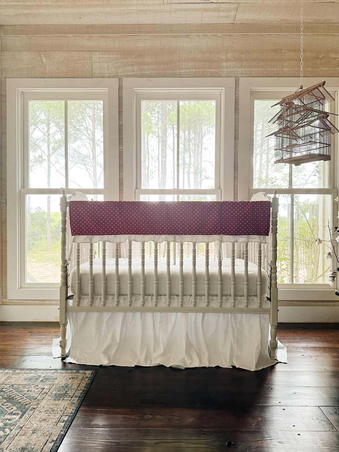 The two-piece red polka dot crib set in a pine-paneled nursery with three windows and a hanging birdcage