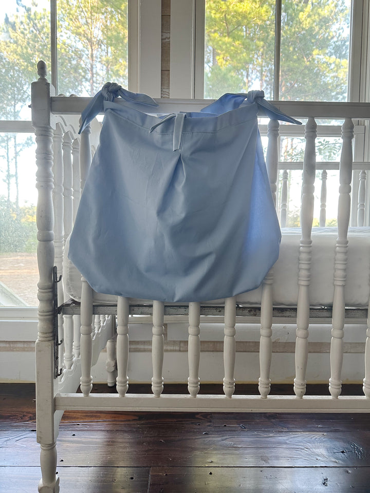 Front of the baby blue cotton caddy hanging over the crib spindles, the pleat running down the middle