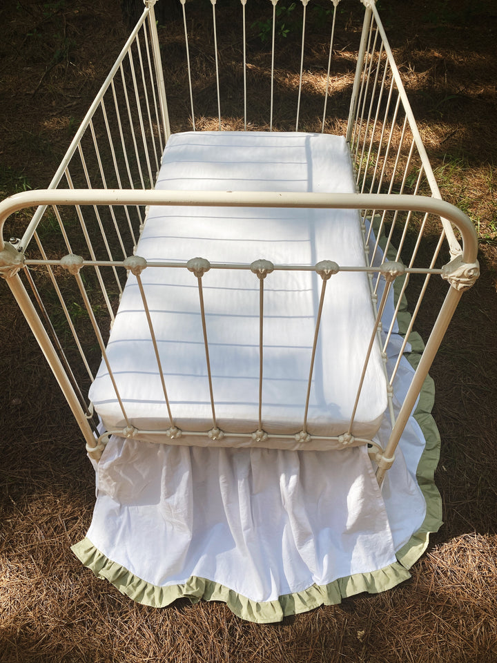 Bird's-eye view of white and sage ruffled crib skirt on iron crib outdoors, all-sided coverage visible