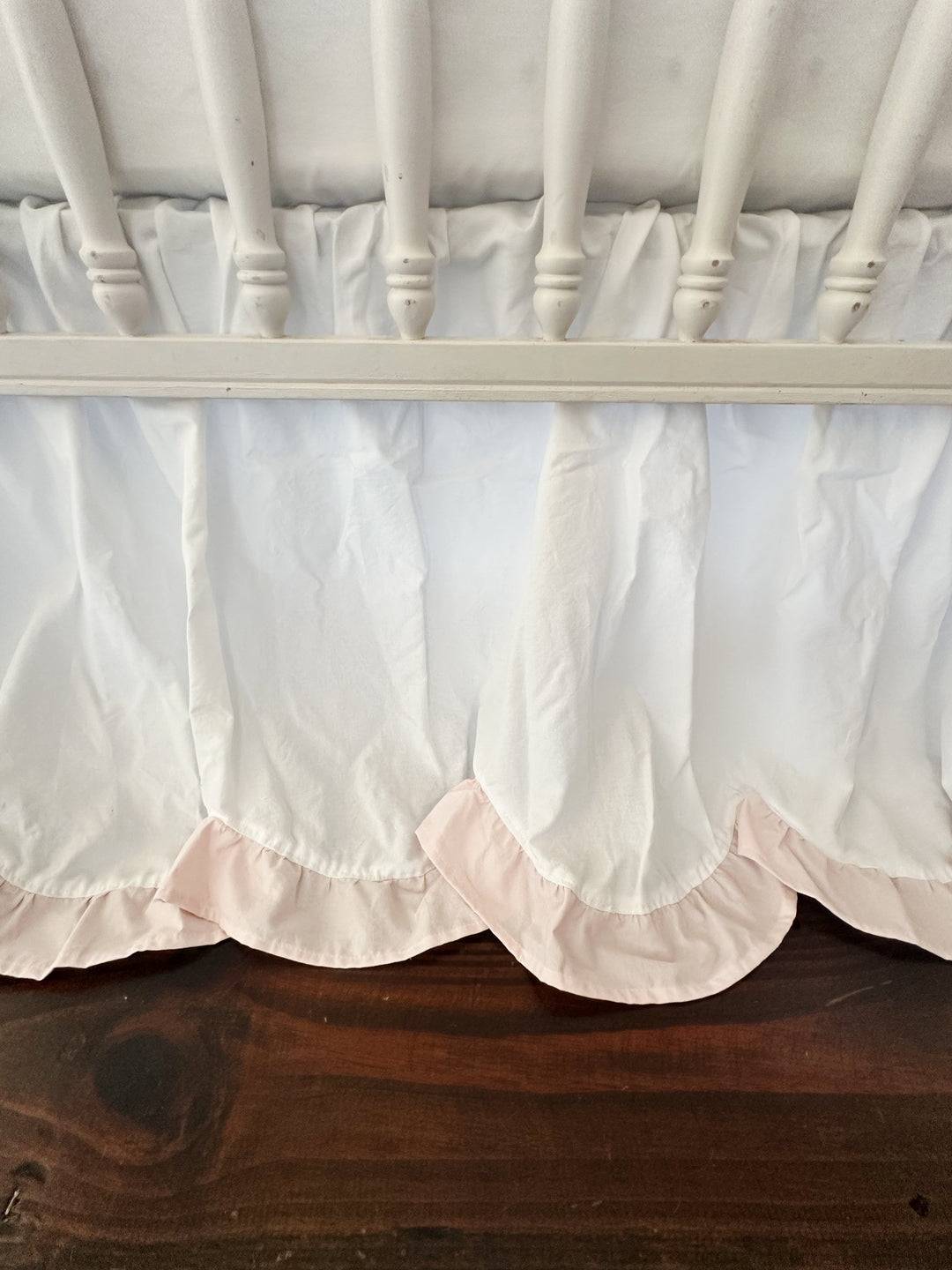 Close view of the scalloped hem and its baby pink ruffle curving beneath the crib rail