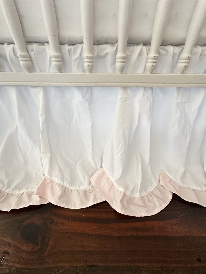 Close view of the scalloped hem and its baby pink ruffle curving beneath the crib rail