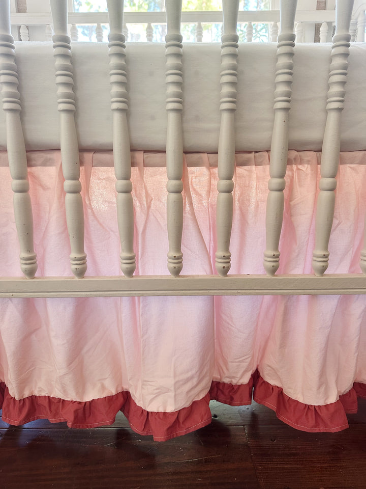 Close-up through the crib spindles: gathered Sisters Pink cotton skirt ending in a blush ruffle just above the wood floor