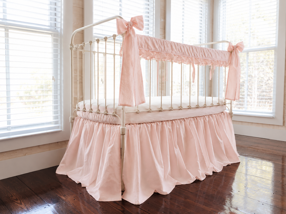 Angled view of the Ballet Slipper Pink crib set in a sunlit nursery with tall windows and dark plank floors