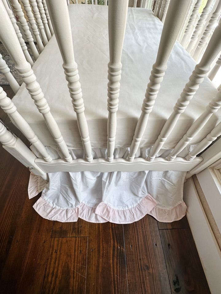 Looking down into the foot end of the crib with the scalloped skirt hanging below the rail