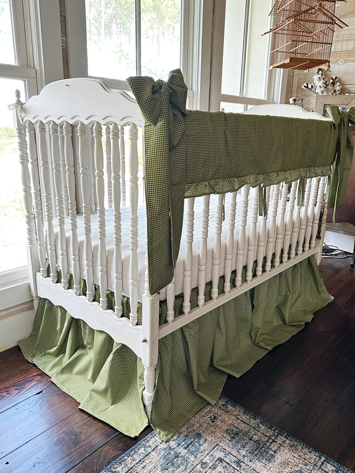 Angled view of green gingham crib rail cover and 20 inch farmhouse crib skirt on a white crib