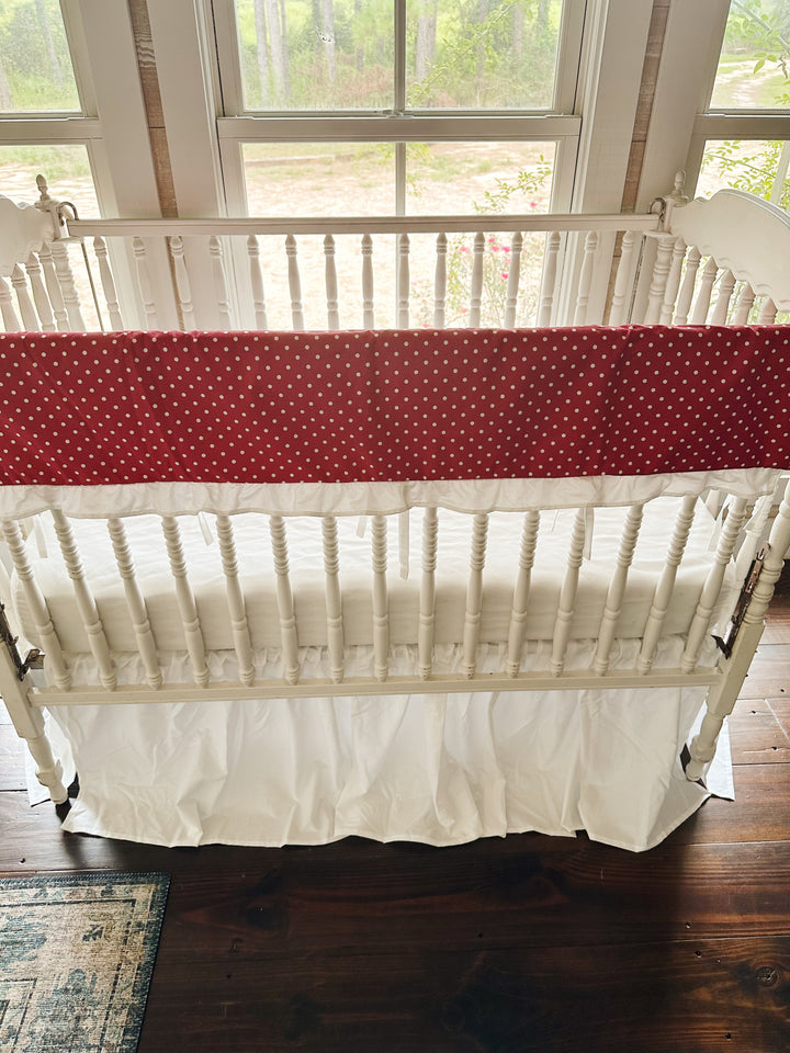 Red and white polka dot ruffled crib rail cover above a gathered white farmhouse crib skirt, no bows on the posts