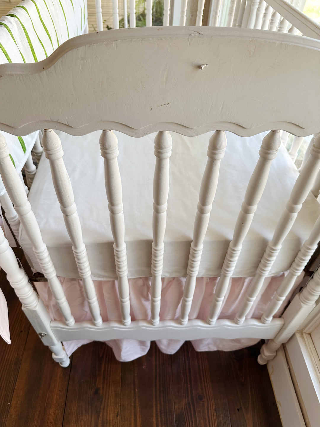 The scalloped headboard and turned spindles above the gathered baby pink crib skirt