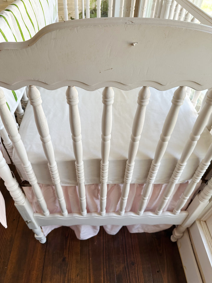 The scalloped headboard and turned spindles above the gathered baby pink crib skirt
