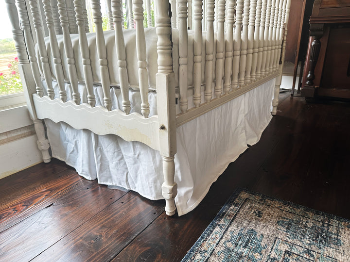 Split corner detail on white tailored crib skirt wrapping around spindle crib leg