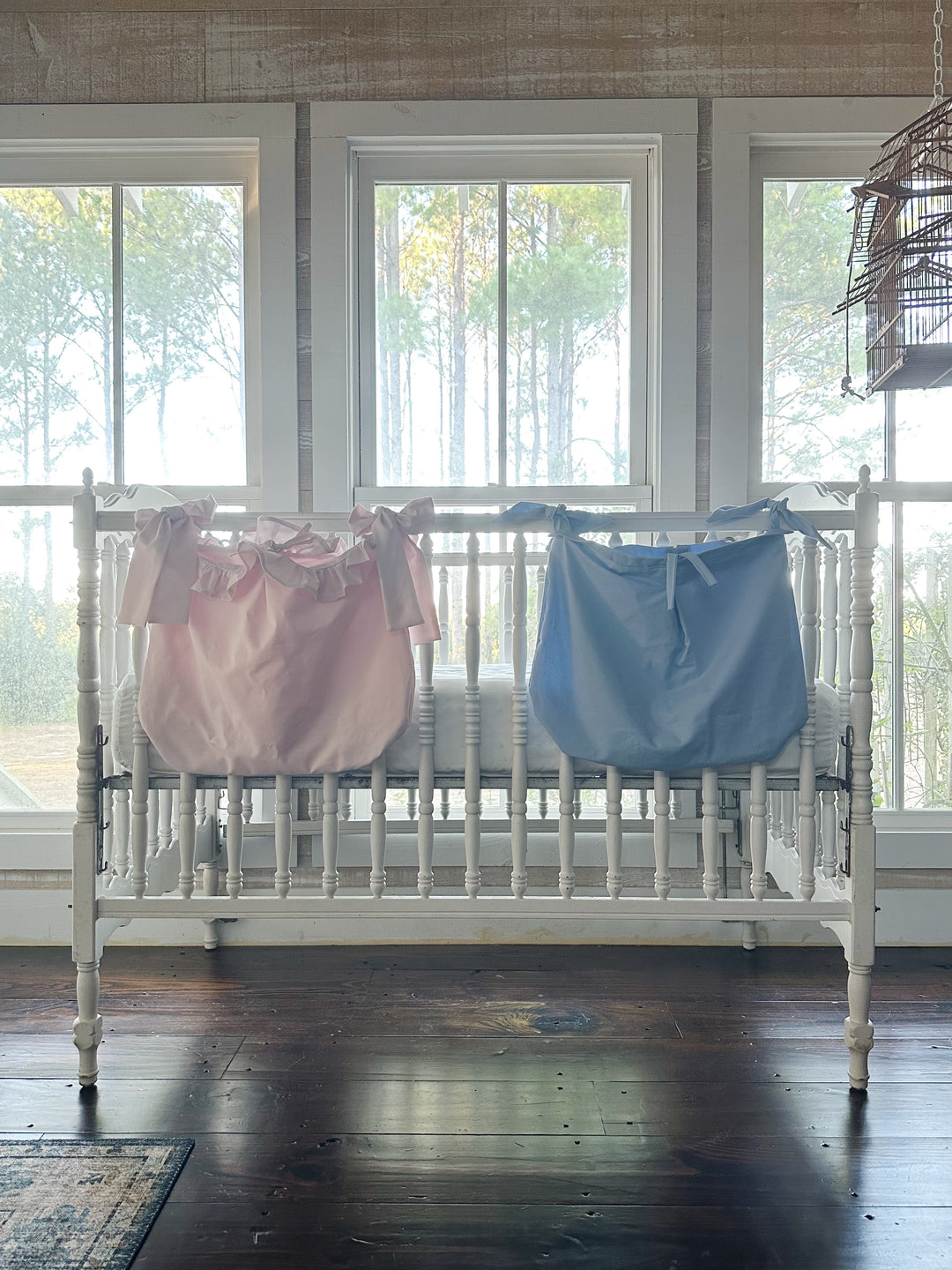 Baby blue tailored caddy hanging beside the baby pink ruffled caddy on a white crib