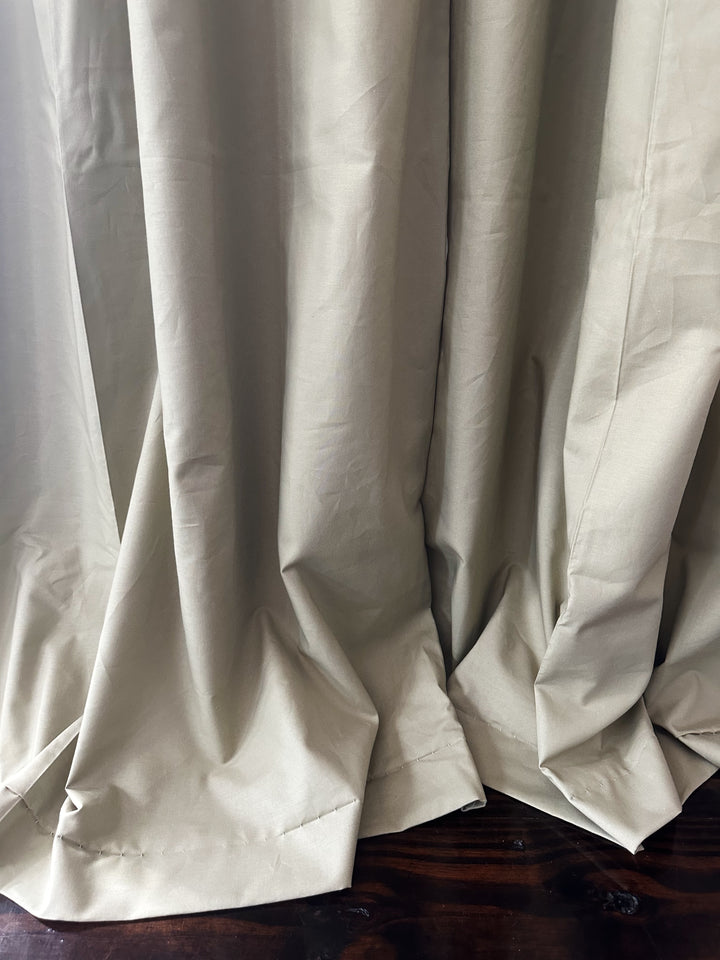 Hem of the sage green blackout curtains folding onto a dark stained wood floor, showing the hand-finished bottom hem