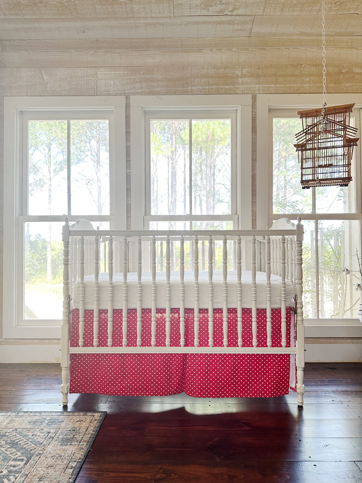 The crib and its red polka dot skirt seen across the room, a birdcage hanging at the right
