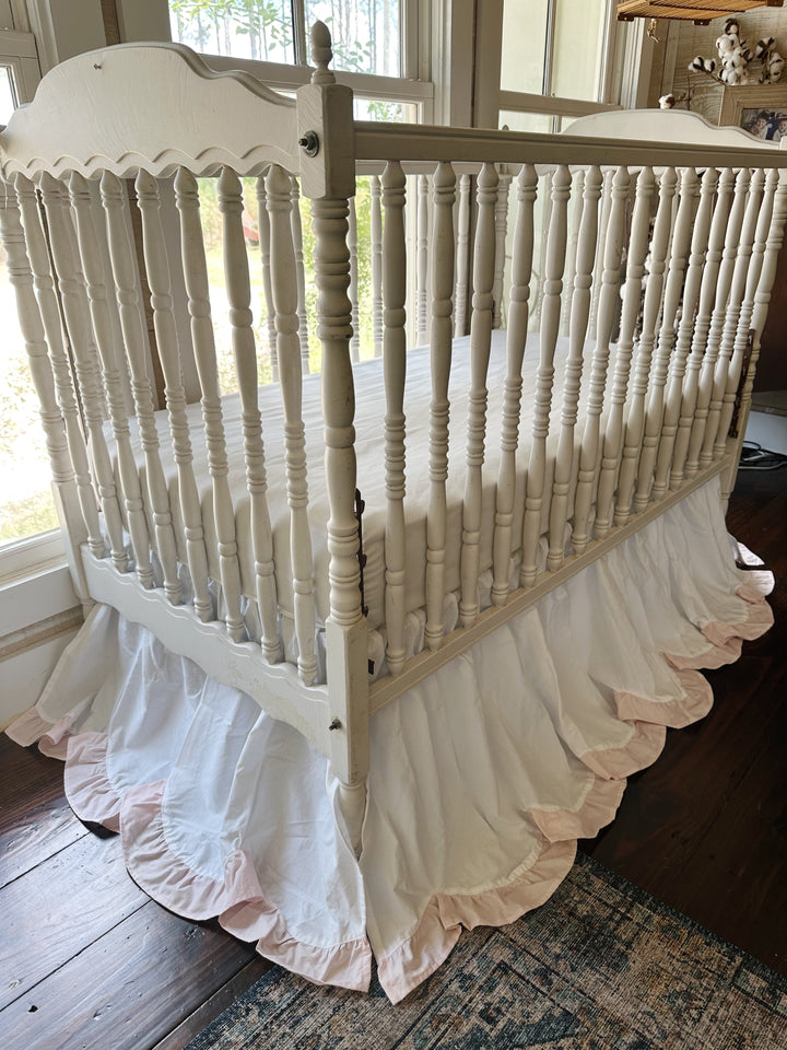 Angled view of the dressed crib with the scalloped skirt reaching the wood floor