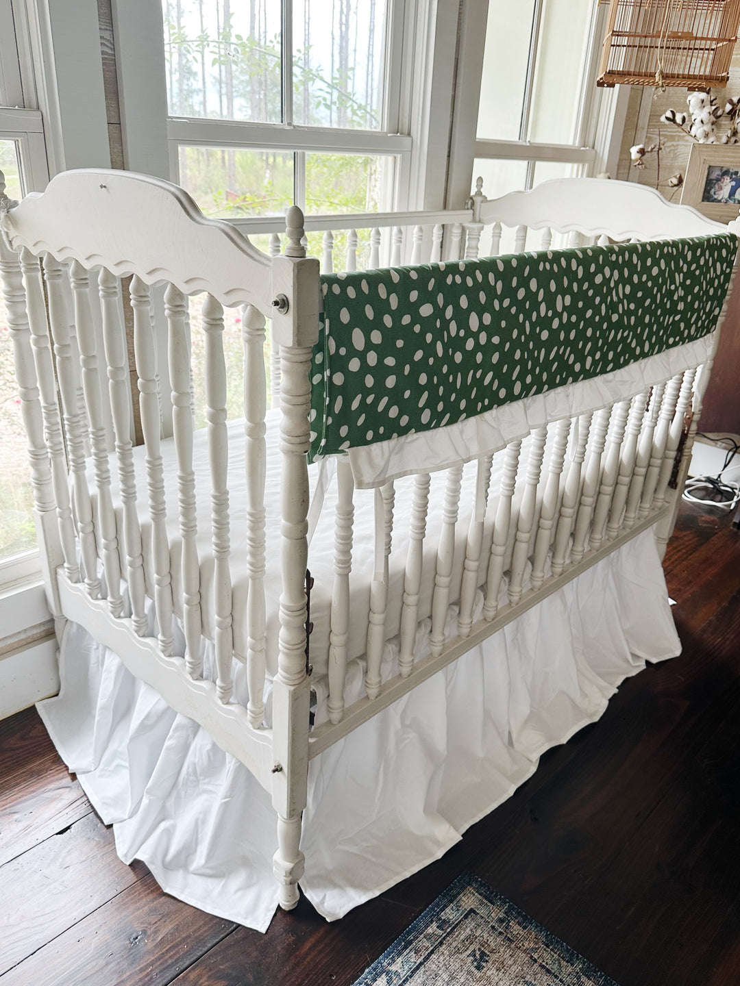 Corner view of the green dot rail cover running down the long rail of a white spindle crib