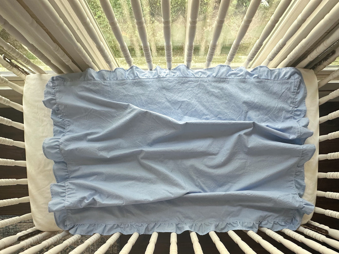 Overhead view of a baby blue ruffled crib blanket spread across a standard crib mattress - High Cotton Textile