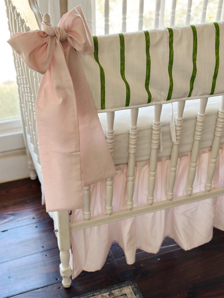 Large pink bow tied over the crib finial, its tails falling past the pink skirt