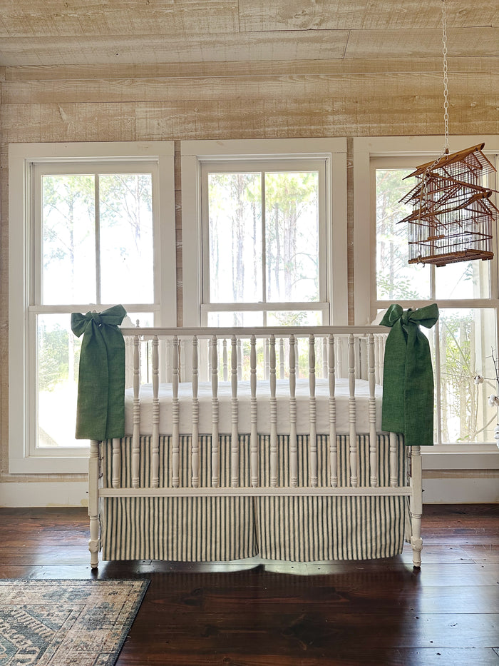 The whole crib across the room, green sashes at each front post above the striped skirt