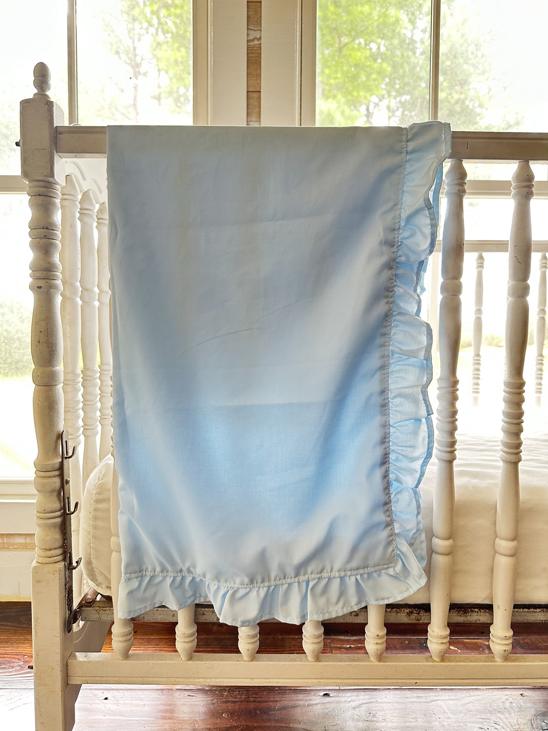 Light blue ruffled baby blanket in washed cotton hanging on a white crib rail - High Cotton Textile