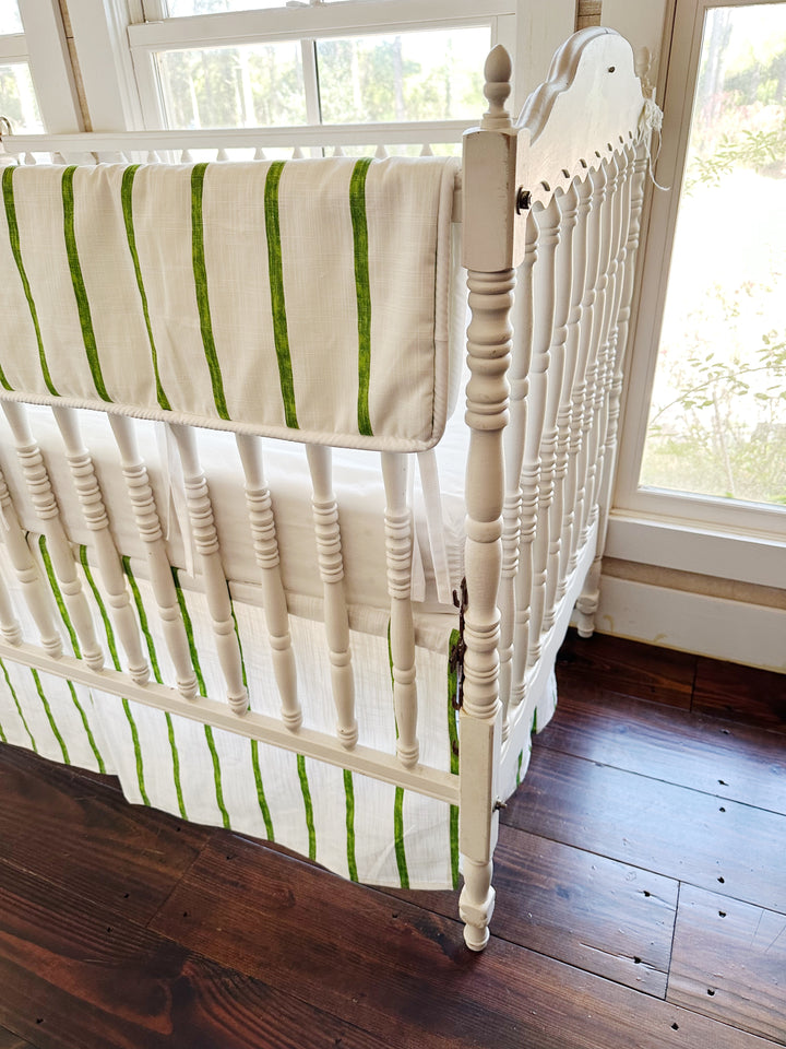 The striped rail cover folded over the long rail, seen from the foot of the crib