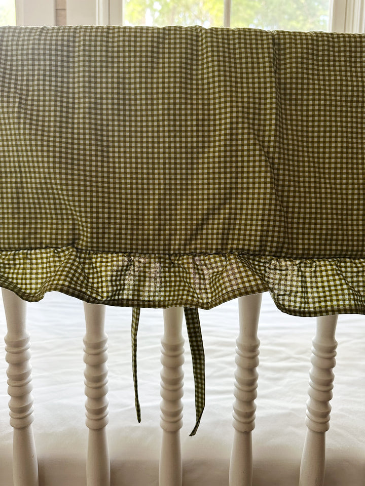 Ruffle edge and tiny fabric ties on the green gingham crib rail cover, backlit by a window