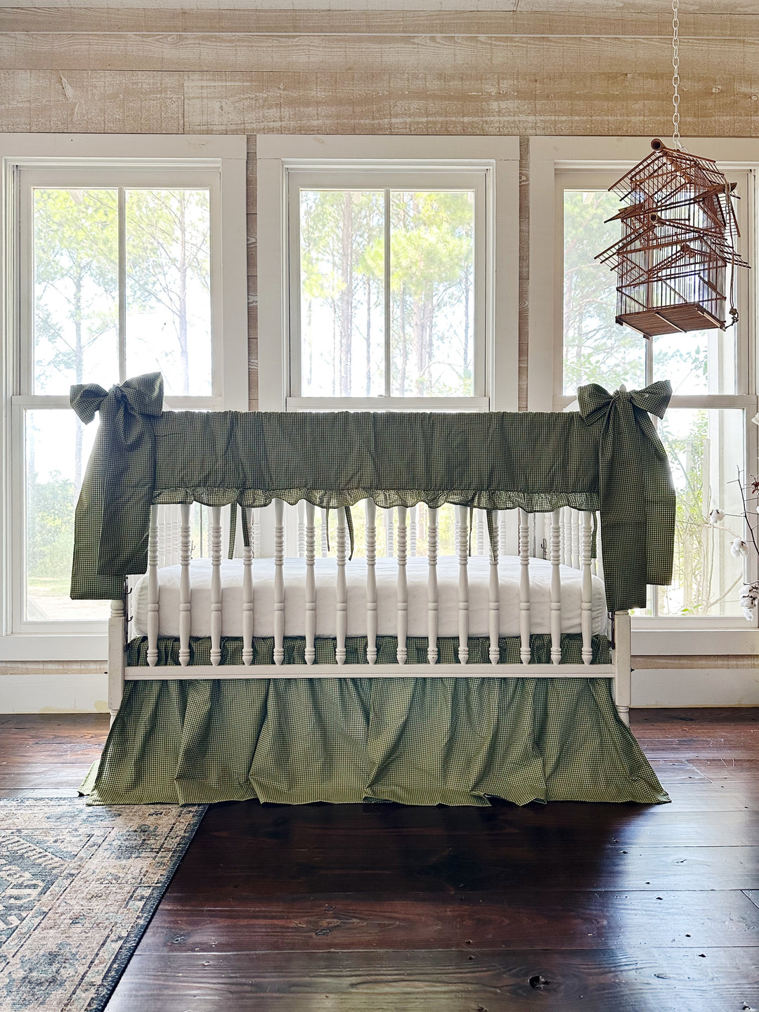 Pine green gingham crib rail cover, farmhouse skirt and two large bows on a white spindle crib