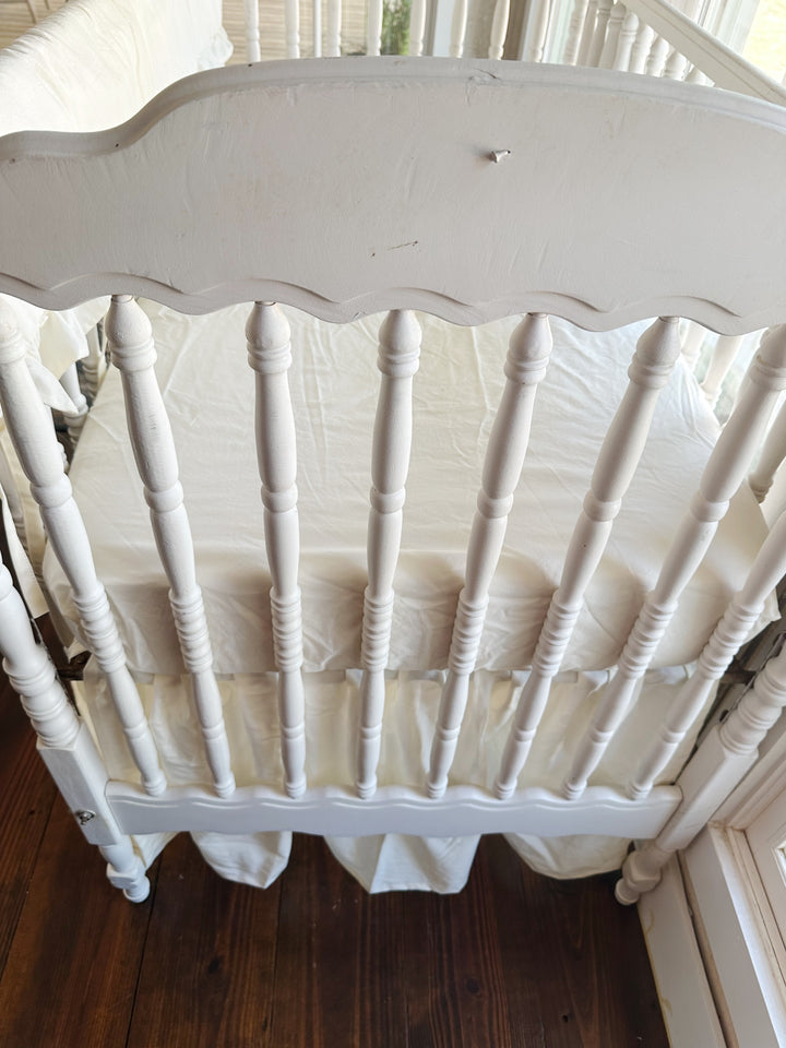 Close overhead view of the scalloped headboard spindles with the ivory skirt gathered beneath the mattress