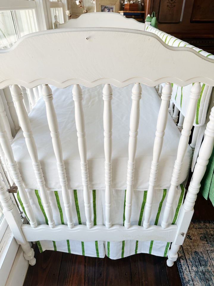 Head end of the crib from above, scalloped headboard and white sheet over the striped skirt