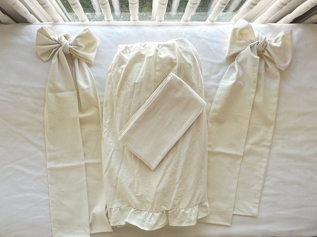 Porcelain ruffled crib skirt panel laid flat between two tied porcelain crib bows with long sash tails