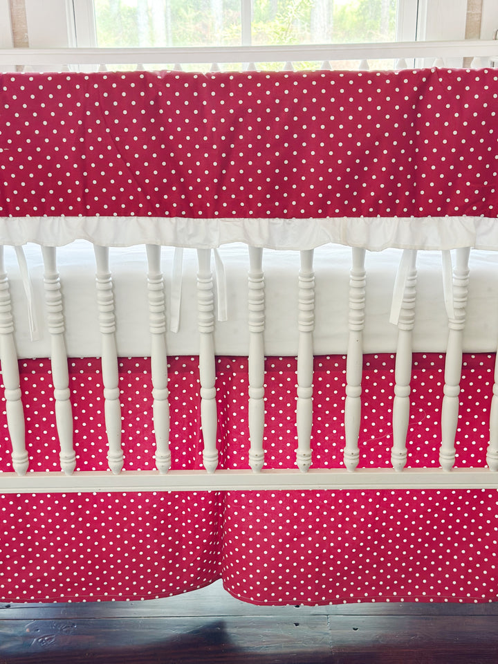 The white ruffle along the bottom of the rail cover with the pleated dotted skirt below