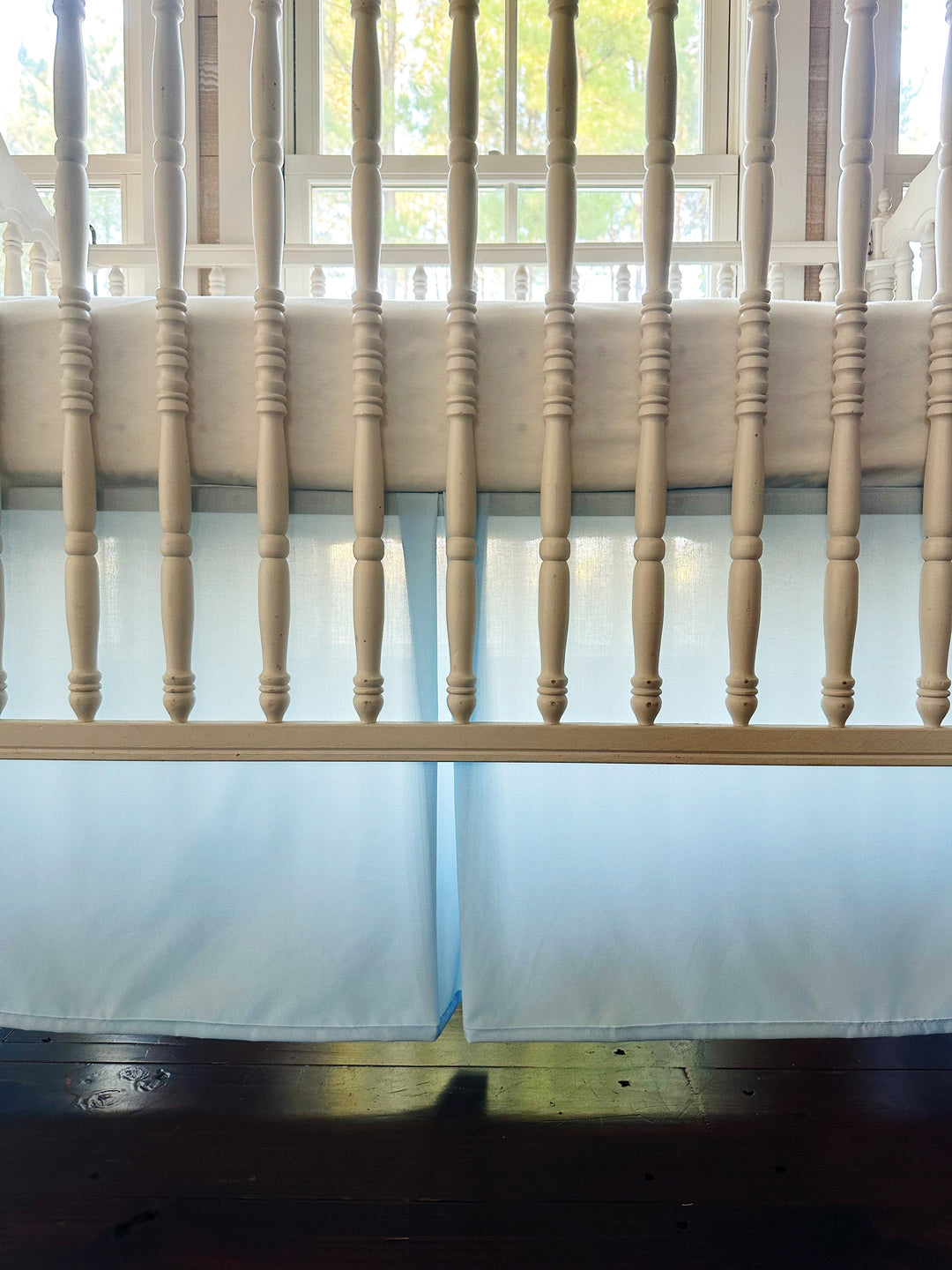Close up through the crib spindles of the heirloom blue skirt's pleated center panel, backlit by a sunny window - High Cotton Textile
