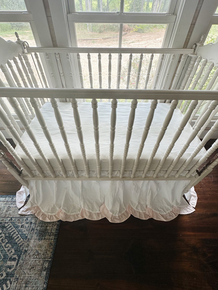 Overhead front view of the crib showing the scalloped hem and pink ruffle across the front panel