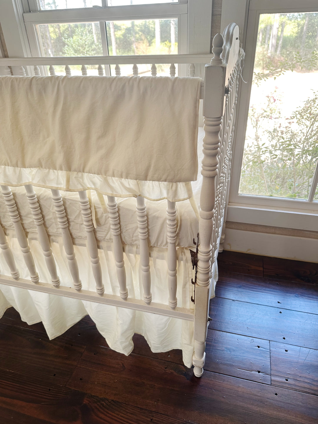 Close view of the ivory rail cover's ruffled edge and fabric ties at the corner post, gathered skirt falling to the floor