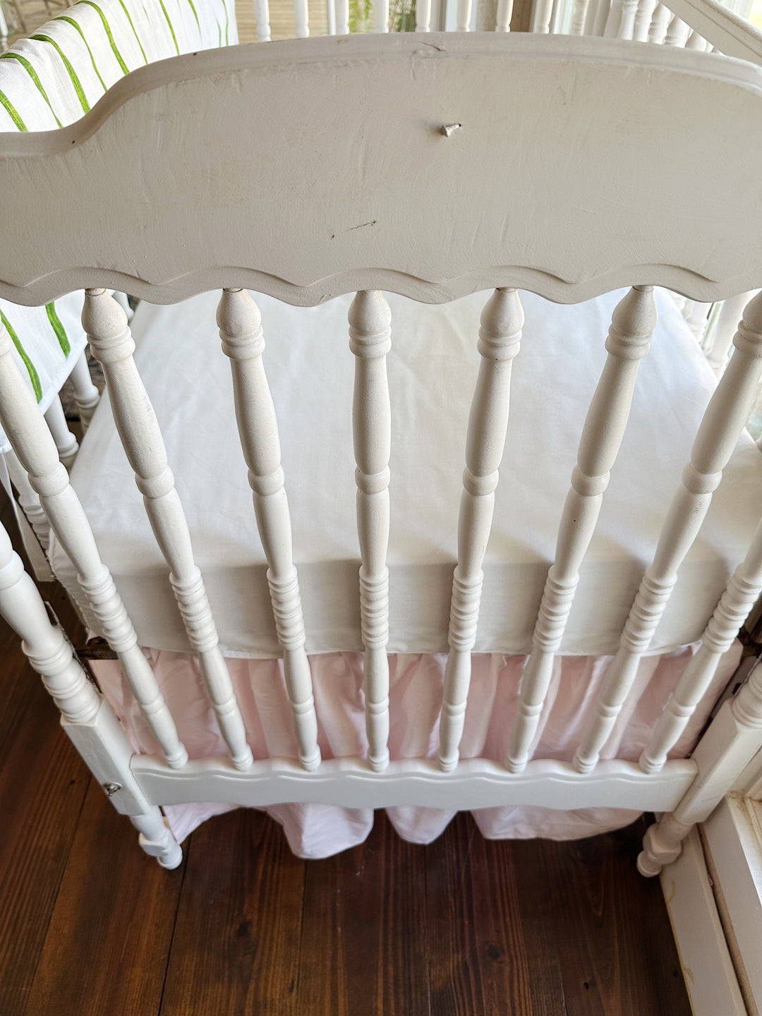 The scalloped headboard and turned spindles above the soft pink farmhouse skirt