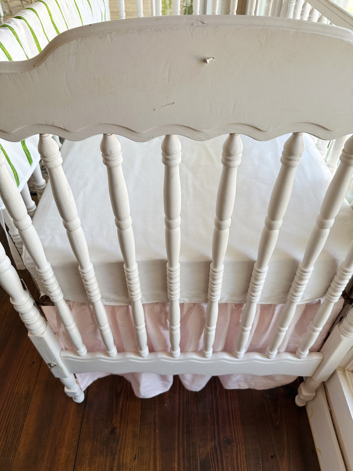 The scalloped headboard and turned spindles above the soft pink farmhouse skirt